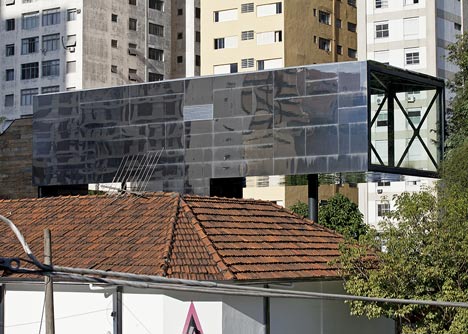 Shiny metal box hovers above shopping and restaurant complex by Triptyque