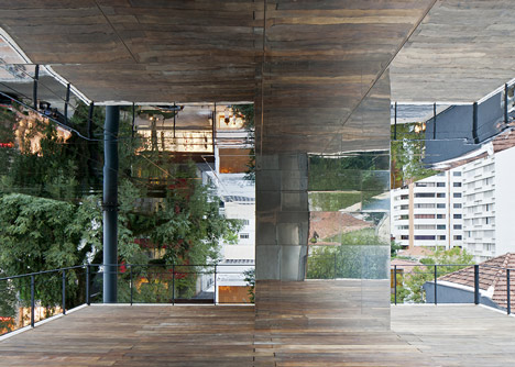 Shiny metal box hovers above shopping and restaurant complex by Triptyque