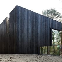 Charred timber and glass villa by VVKH Architecten is embedded in a sand dune