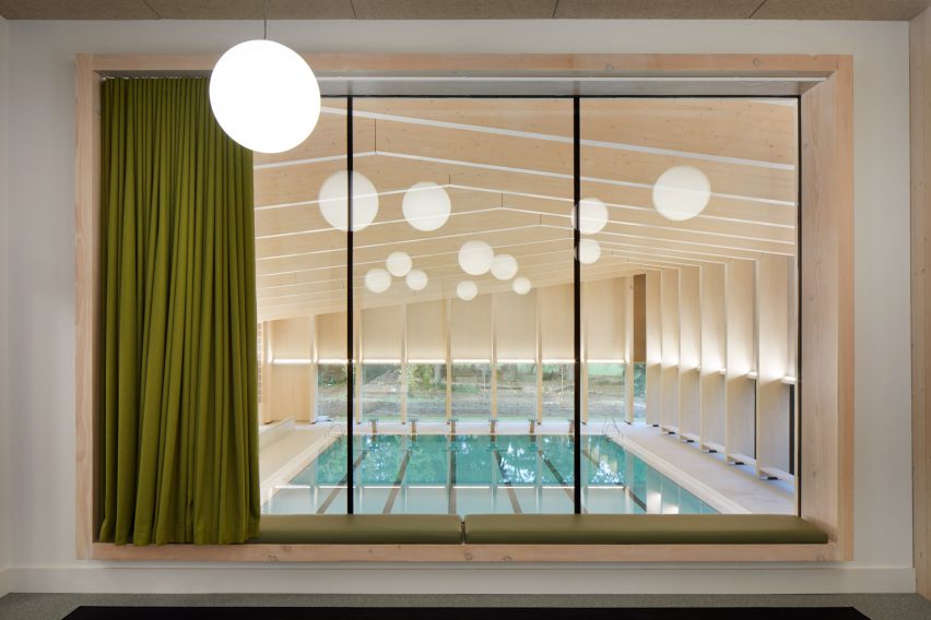 British firm Hawkins\Brown has completed a swimming-pool building at a school in Surrey, England, featuring an exposed timber frame that incorporates windows looking out onto the surrounding woodland.
