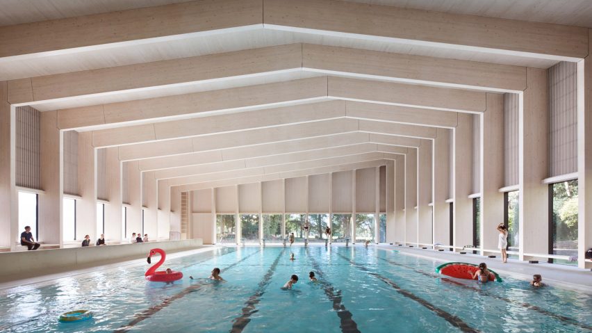 British firm Hawkins\Brown has completed a swimming-pool building at a school in Surrey, England, featuring an exposed timber frame that incorporates windows looking out onto the surrounding woodland.