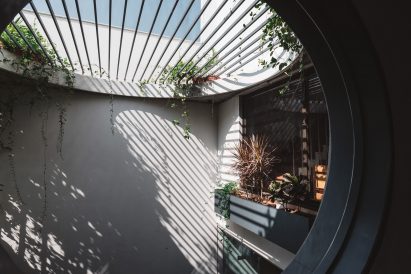Living spaces at this house in the Indian city of Surat are arranged around a verdant courtyard lined with glass walls that can be retracted to open the interior up to the outdoors