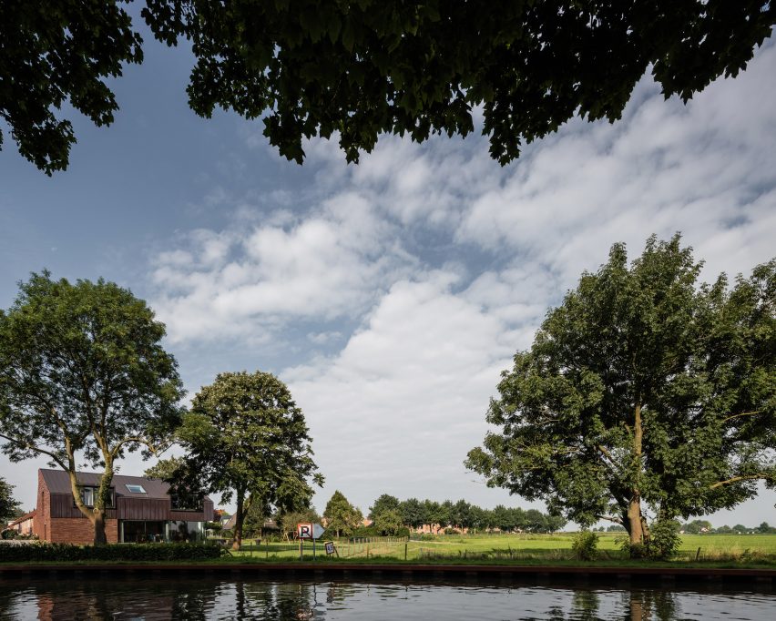 Villa IJsselzig by EVA Architecten is a riverside home featuring red-brick walls and a patinated copper roof
