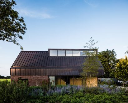 Villa IJsselzig by EVA Architecten is a riverside home featuring red-brick walls and a patinated copper roof