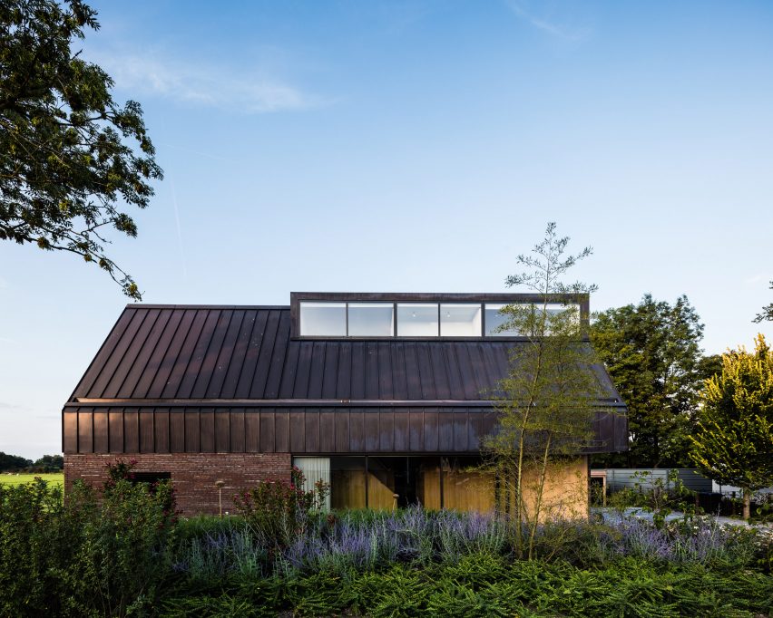 Villa IJsselzig by EVA Architecten is a riverside home featuring red-brick walls and a patinated copper roof