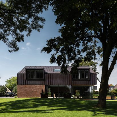Villa IJsselzig by EVA Architecten is a riverside home featuring red-brick walls and a patinated copper roof