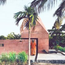 Red concrete meditation space sits under pyramidal roof in rural India