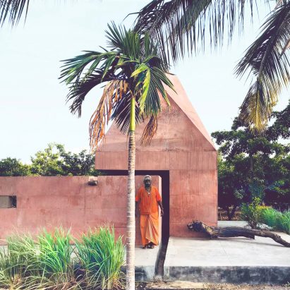 Red concrete meditation space sits under pyramidal roof in rural India