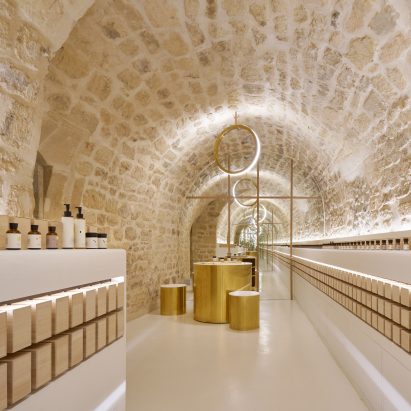 Old stone contrasts with polished brass inside En skincare store in Paris by Archiee