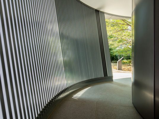The toilet is surrounded by a wall made from metal louvres