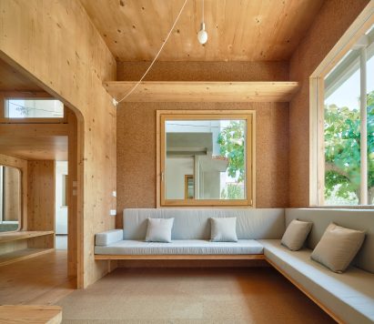 Built in sofa with pale upholstery sits below large square windows by Aixopluc