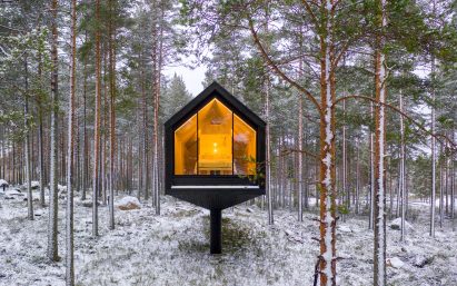 A black cabin elevated on a column in Finnish woodland