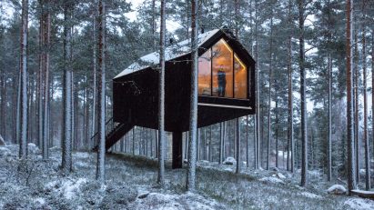A black-painted cabin elevated in woodland in Finland