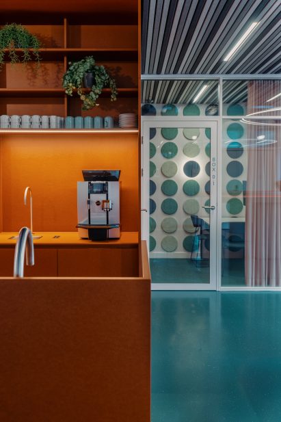An orange kitchen with silver hardware sits atop green flooring