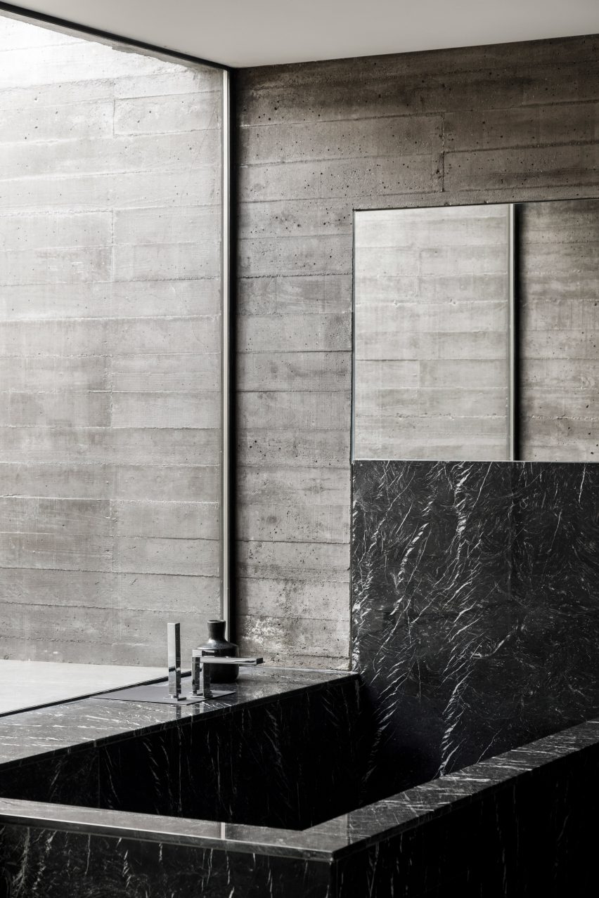 A concrete bathroom with a black stone bathtub