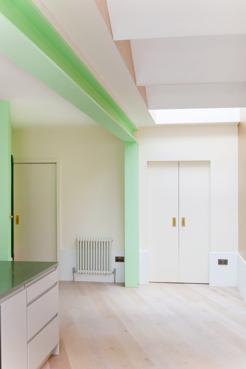 A white kitchen with green structural beams and a wooden floor
