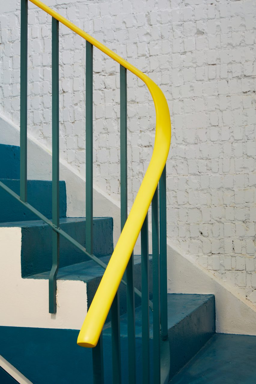 A teal-hued staircase with a yellow banister