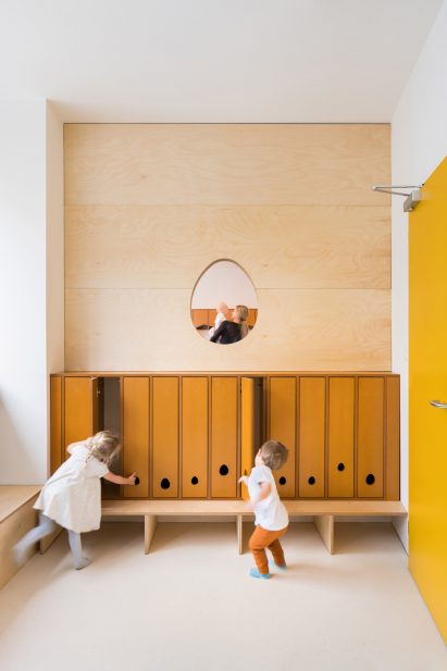 Mustard-coloured cloak room with egg-shaped window in Malvína Day Nursery