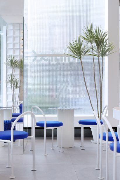 Reeded glass windows and white steel seating in tea shop by Raams Architecture Studio