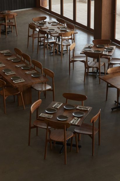 Wooden dining tables and chairs on concrete floor in Three Blue Ducks restaurant by Pattern