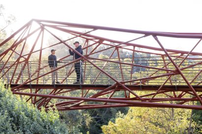 Two people stand on a bridge across a canyon