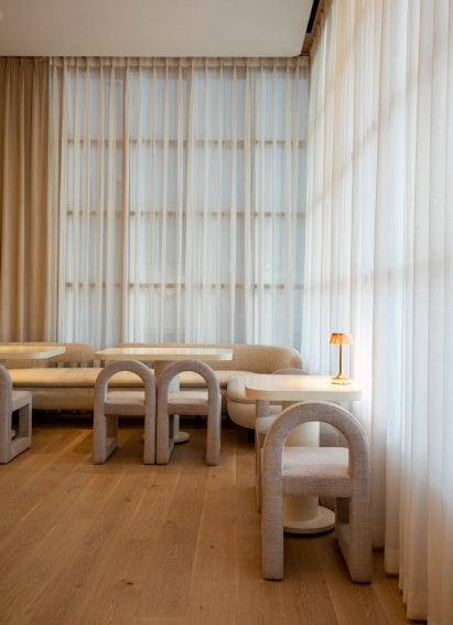 Seating area with sheer curtains and rounded seating in restaurant by Ashiesh Shah