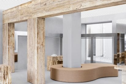 Travertine wall, mirrored clothes rail and upholstered bench in Axel Arigato Paris store