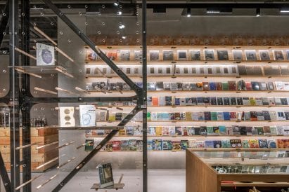 Illuminated shelving with books and clear divider with wooden dowels in retail interior by LUO Studio