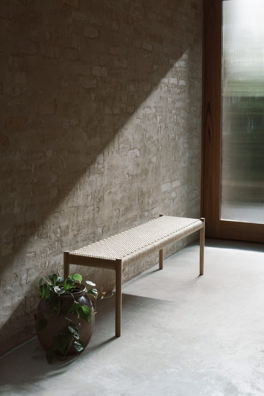 A wooden bench against a pale brick wall