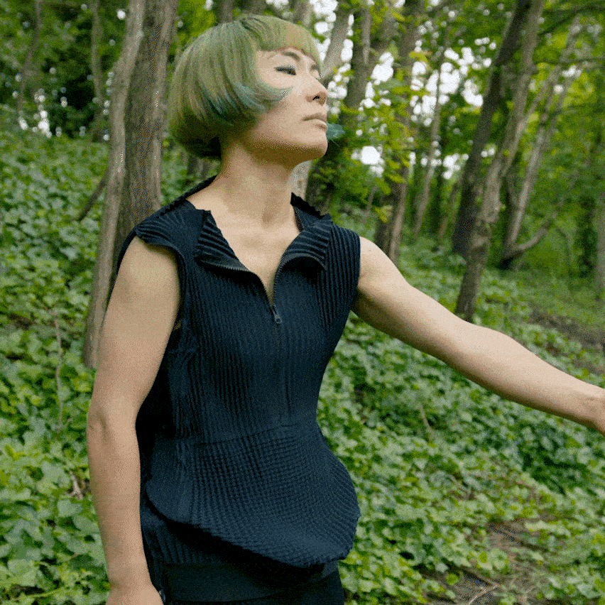 A woman in a green forest stretches her Petit Pli clothing