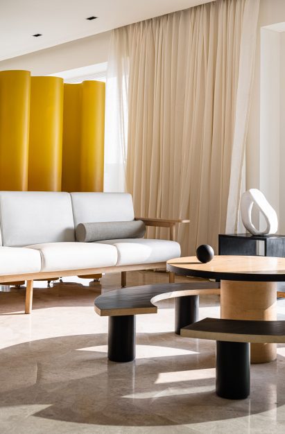 White couch with wooden coffee table and curved bench by The Act of Quad