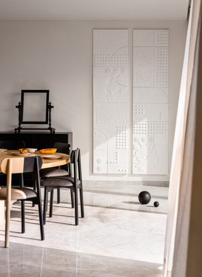 Dining table setup next to white gypsum artwork and black sphere on the floor in Mumbai apartment