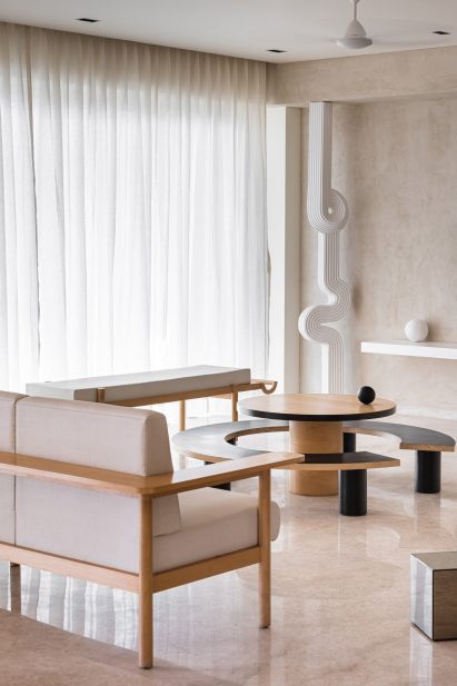 Sofas around a round coffee table with a curved bench and a winding column in Mumbai apartment