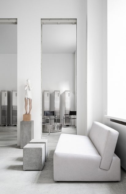 Beige sofa with concrete plinth tables and statue of a boy in tattoo parlour by Balbek Bureau