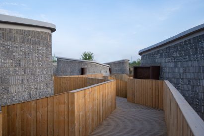 Wooden walkway leading to four vertical pods by AVOID Studio