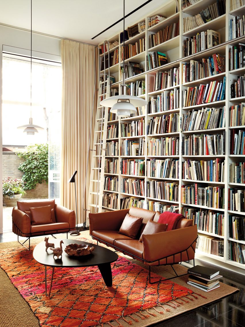Brown leather sofas with a black wire frame next to a coffee table with an egg shaped top in a book-lined living room