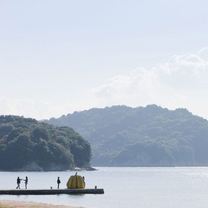 A yellow and black pumpkin sculpture on the edge of a pier