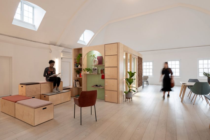Pale wood-panelled meeting room module in an open workplace with arched shelving and lockers decorating its exterior