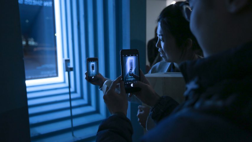 People looking through smartphones into an illuminated glowing blue display case