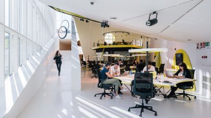 A sunlit room contains students studying and a figure descending a ramp