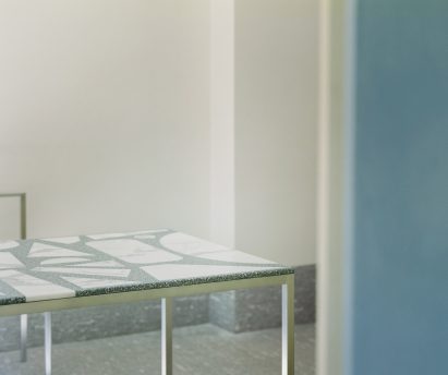 Dining table with green top embedded with large pieces of waste stone