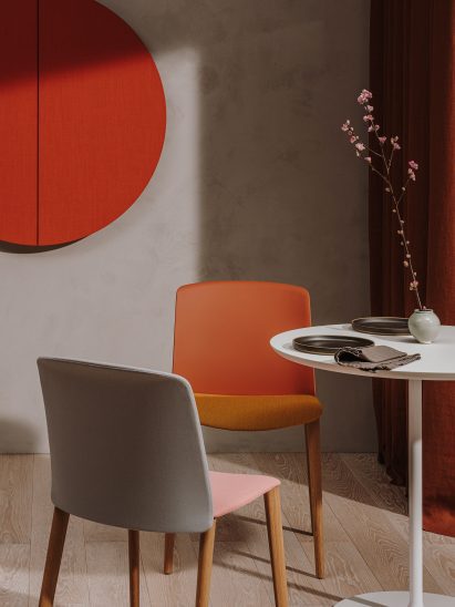 Forward-facing red Mixu chair shown with the back of a grey and pink Mixu chair, surrounded by a table with flowers on it