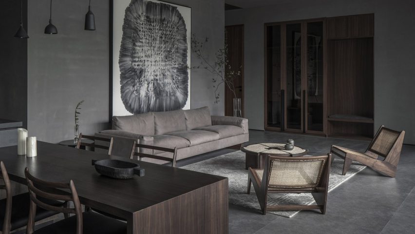 Seating area with grey sofa and wooden rattan chairs in guest room of hotel by Gad Line+
