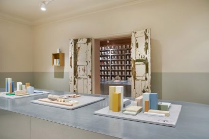 Colourful blocks in different shapes fit on a steel table, with a decaying door leading to a roomful of paint tins in the background