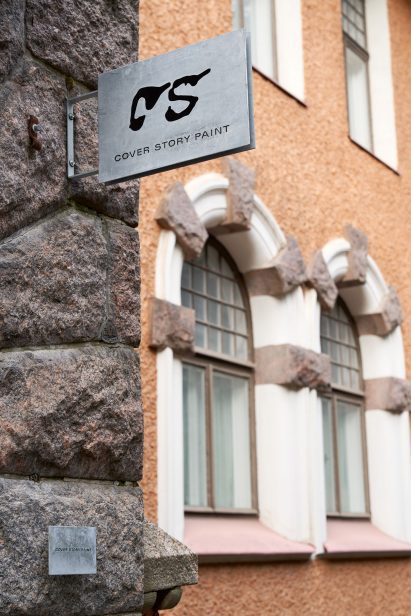 Cover Story metal sign hanging from the stone wall outside of a Helsinki building