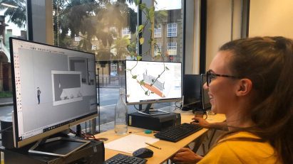 Student using architectural software on a desktop computer by a window