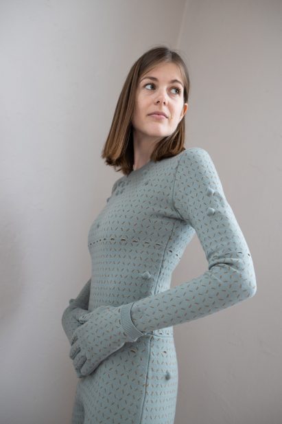 Woman wearing light teal bodysuit with matching gloves with a grid pattern stitched into it and massage balls inside the grid