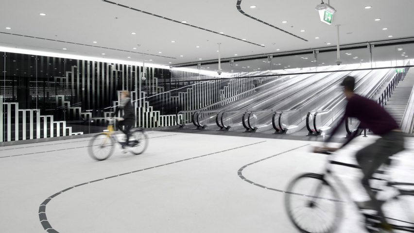 Two people cycle inside a white parking garage