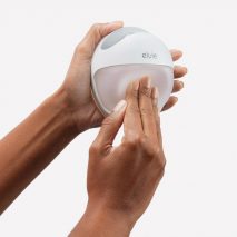 Female hands pressing down on a Elvie Curve silicone breast pump