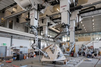 Robotic arms hold geometric wooden panels together in a warehouse
